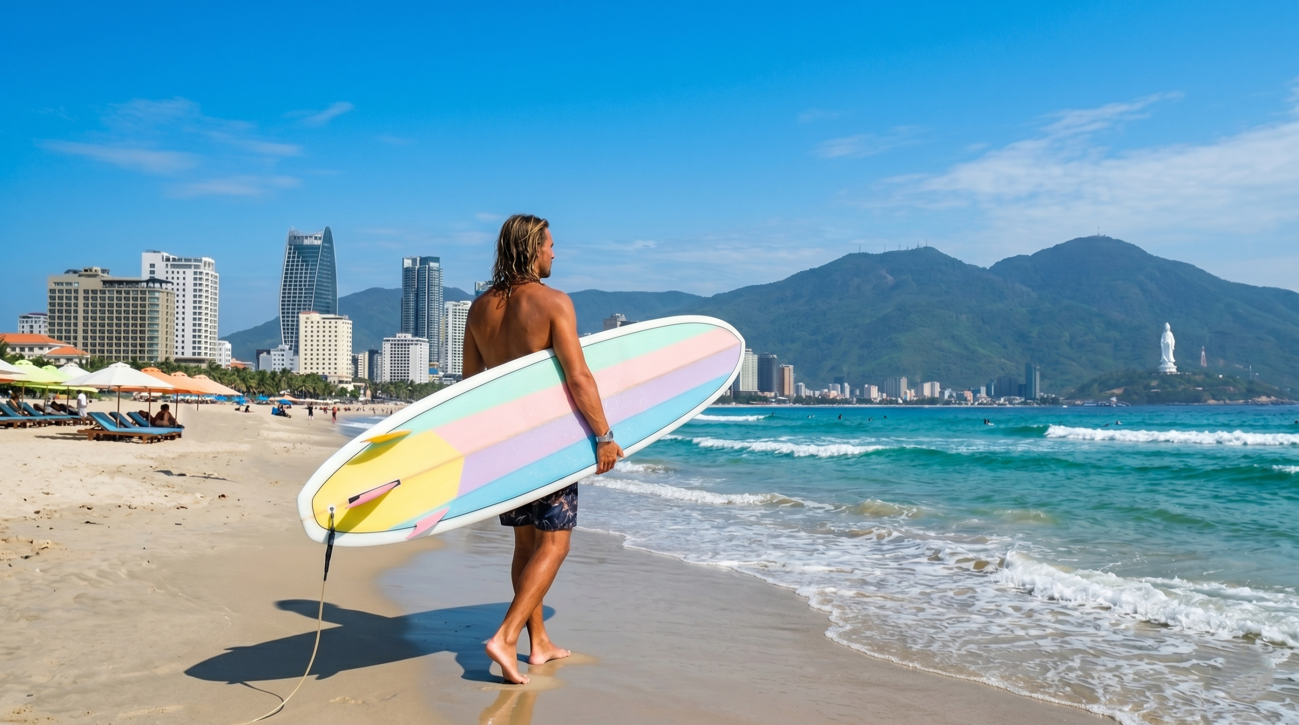 A surfer walking on My Khe beach holding a pastel lilac and pink surfboard from a Da Nang surfboard rental shop, with the city skyline and mountains in the background